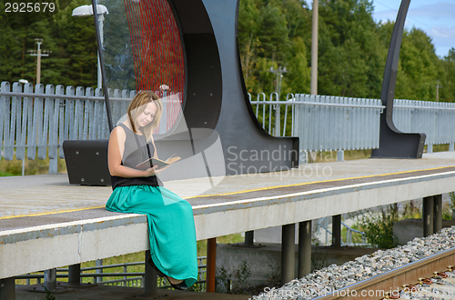 Image of Young female sitting on the station and reading