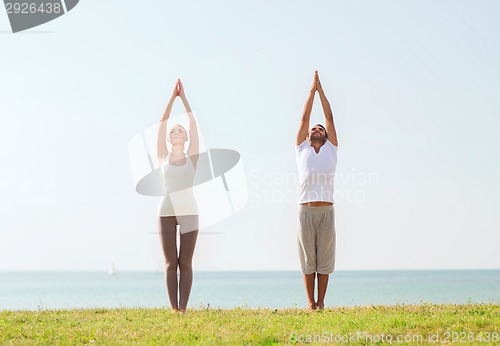 Image of smiling couple making yoga exercises outdoors