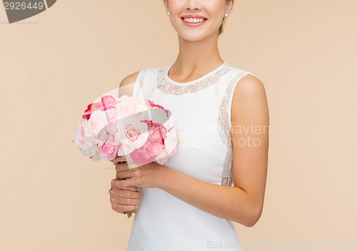 Image of smiling woman in white dress with bouquet of roses