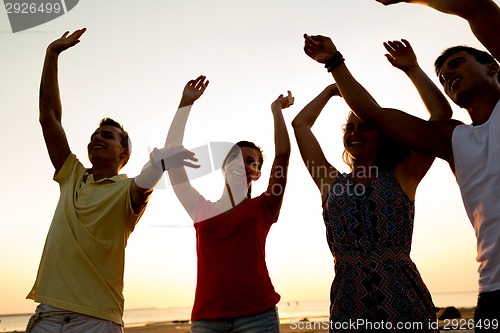 Image of smiling friends dancing on summer beach