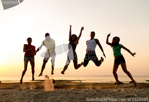 Image of smiling friends dancing and jumping on beach