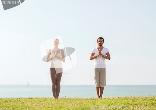 Image of smiling couple making yoga exercises outdoors