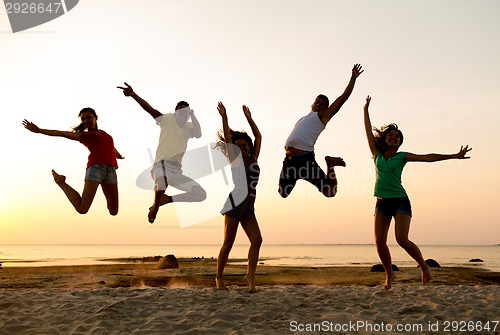 Image of smiling friends dancing and jumping on beach