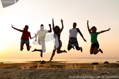 Image of smiling friends dancing and jumping on beach