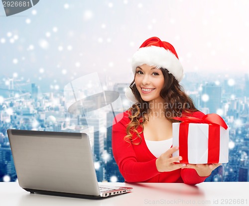 Image of smiling woman in santa hat with gift and laptop