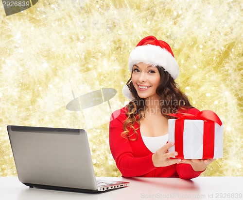 Image of smiling woman in santa hat with gift and laptop