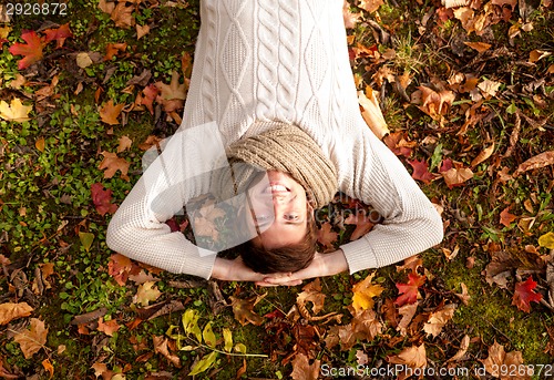 Image of smiling young man lying on ground in autumn park