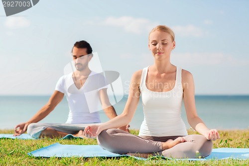 Image of smiling couple making yoga exercises outdoors