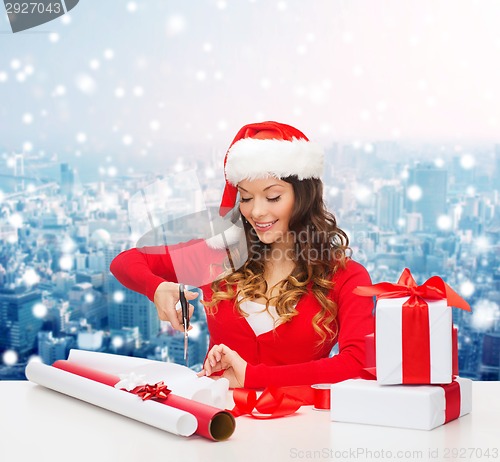 Image of smiling woman in santa helper hat packing gift box