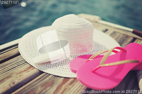 Image of close up of hat, sunscreen and slippers at seaside