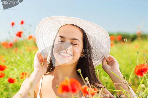 Image of smiling young woman in straw hat on poppy field