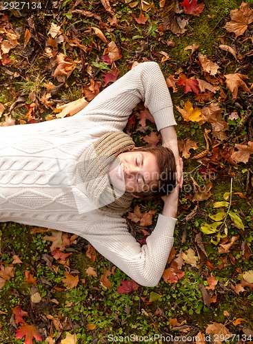 Image of smiling young man lying on ground in autumn park