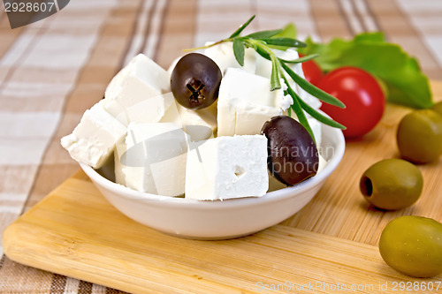 Image of Feta with olives in cup on brown cloth and board