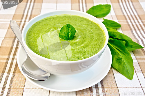Image of Soup puree with spinach and spoon in white bowl on fabric