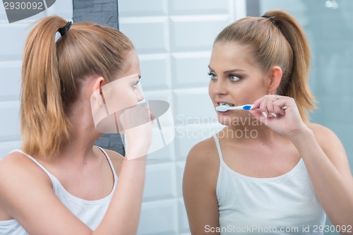 Image of Young woman brushing her teeth in the mirror