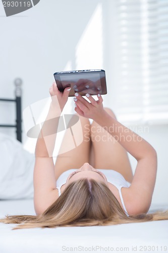 Image of Young woman lying on her bed using a tablet-pc