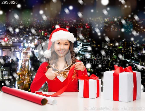 Image of smiling woman in santa helper hat packing gift box