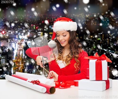 Image of smiling woman in santa helper hat packing gift box