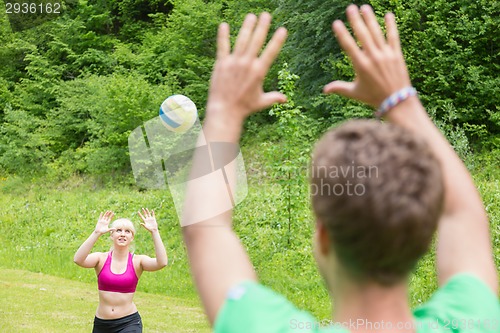 Image of Young couple playing volleyball in park.