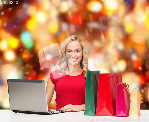Image of smiling woman in red shirt with gifts and laptop