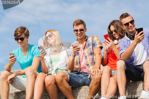 Image of group of smiling friends with smartphones outdoors