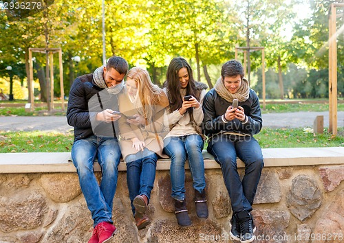 Image of smiling friends with smartphones in city park