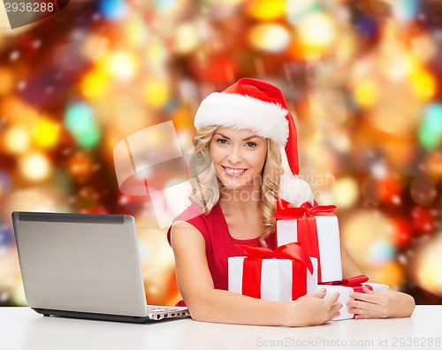 Image of smiling woman in santa hat with gifts and laptop