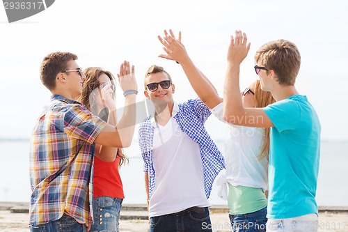 Image of group of smiling friends making high five outdoors