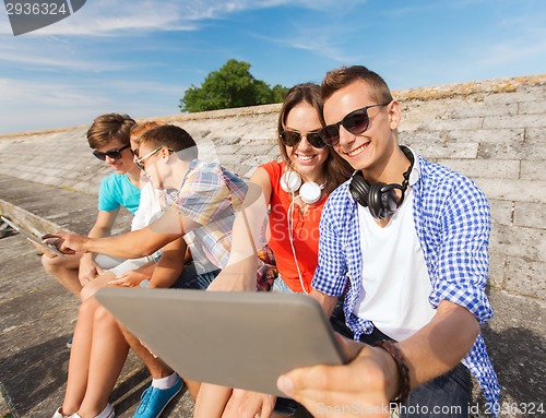 Image of group of smiling friends with tablet pc outdoors