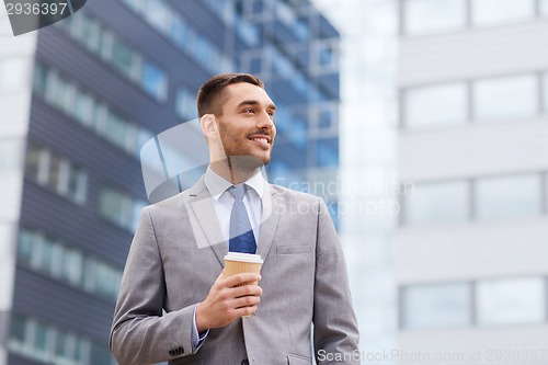 Image of young smiling businessman with paper cup outdoors