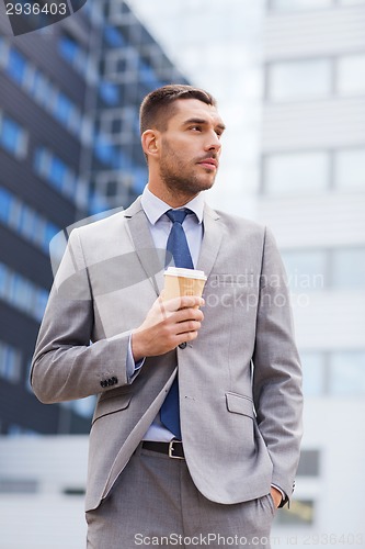 Image of young serious businessman with paper cup outdoors