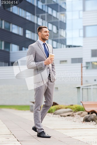 Image of young serious businessman with paper cup outdoors