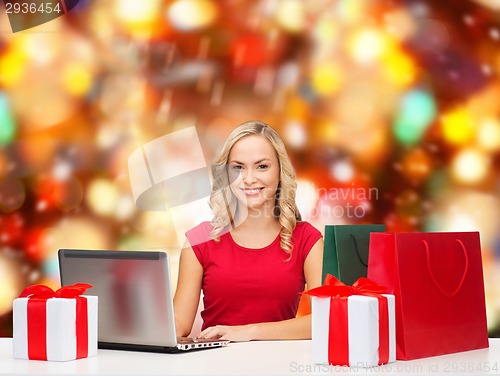 Image of smiling woman in red shirt with gifts and laptop