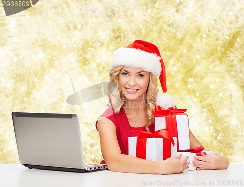 Image of smiling woman in santa hat with gifts and laptop