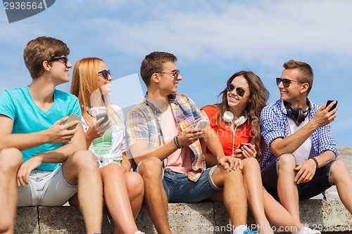 Image of group of smiling friends with smartphones outdoors