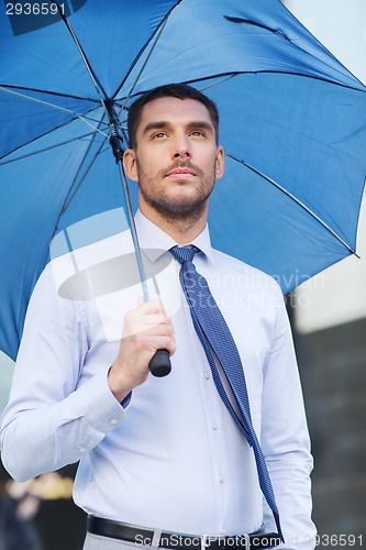 Image of young serious businessman with umbrella outdoors