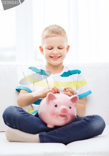 Image of smiling little boy with piggy bank at home