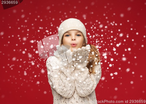 Image of happy girl in winter clothes blowing on palms