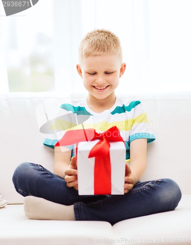 Image of smiling little holding gift box sitting on couch