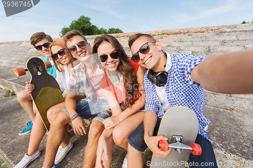 Image of group of smiling friends with smartphone outdoors