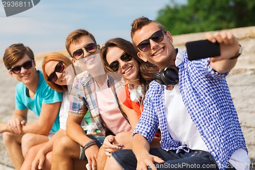 Image of group of smiling friends with smartphone outdoors