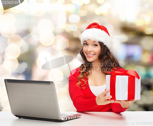 Image of smiling woman in santa hat with gift and laptop