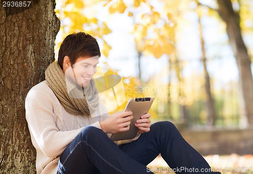 Image of smiling young man with tablet pc in autumn park