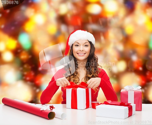 Image of smiling woman in santa helper hat packing gifts