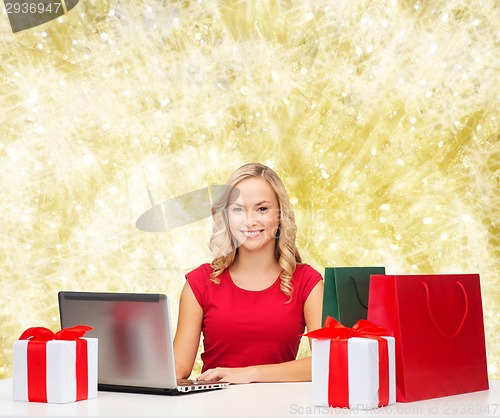 Image of smiling woman in red shirt with gifts and laptop