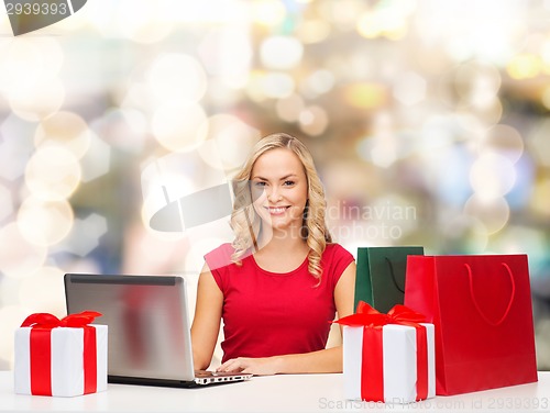 Image of smiling woman in red shirt with gifts and laptop