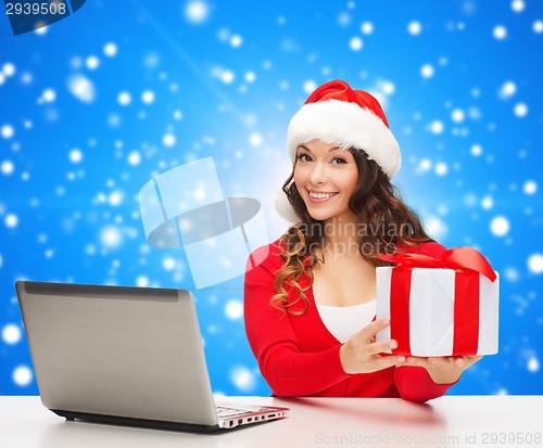 Image of smiling woman in santa hat with gift and laptop