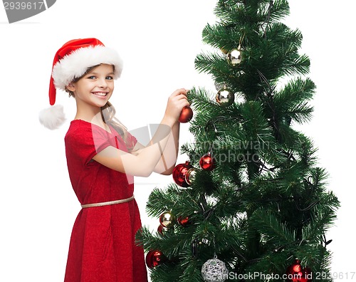Image of smiling girl in santa helper hat decorating a tree