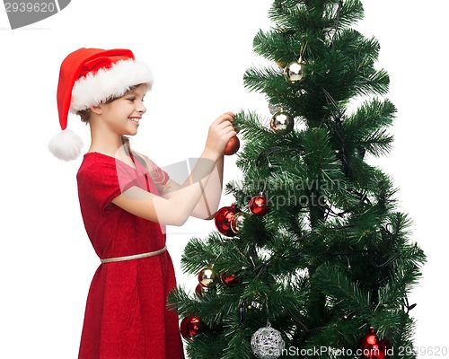 Image of smiling girl in santa helper hat decorating a tree