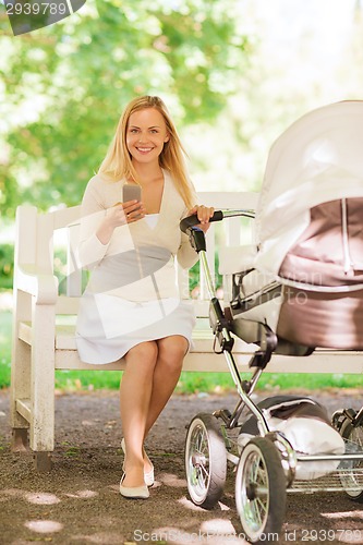 Image of happy mother with smartphone and stroller in park